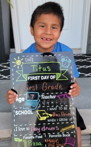 Little boy holding a back to school sign while sitting on a front step.