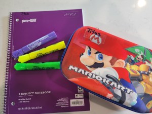 Assorted school supplies, purple notebook, 3 scented markers, and a Mario pencil box.