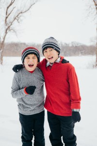 Two boys wearing stocking hats, smiling and laughing in a snowy field.