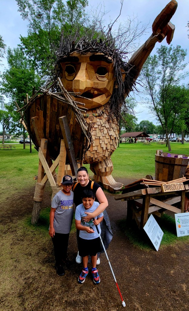 large troll with a mom and two boys standing in front smiling. One boy is holding a white cane.
