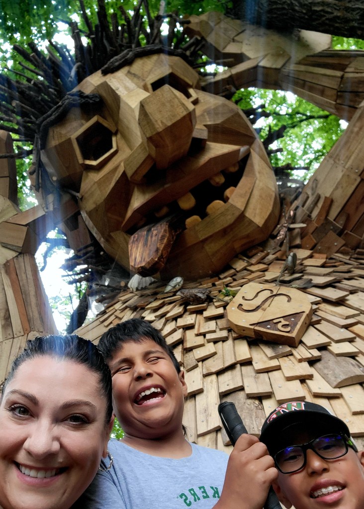 Mom and two boys smile in front of a silly faced troll.