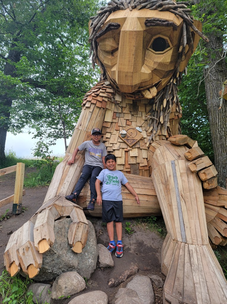 Two boys pose and smile in front of a troll.