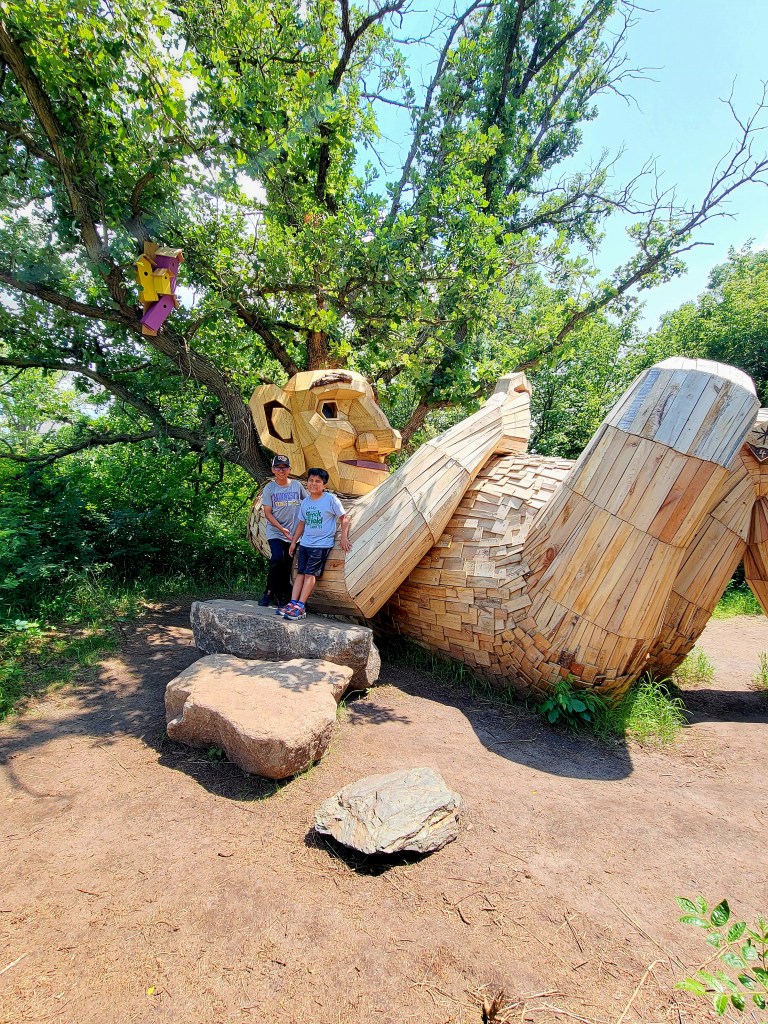 Two boys smile in front of a sleeping troll.
