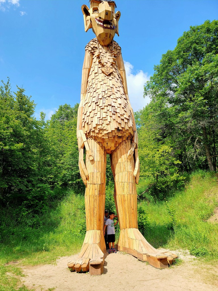 Two boys pose under the body of a very tall troll.