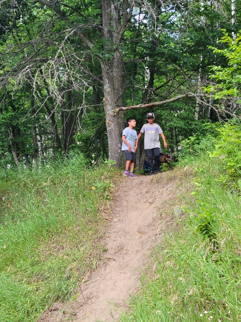Two boys hiking to the top of a dirt hill.