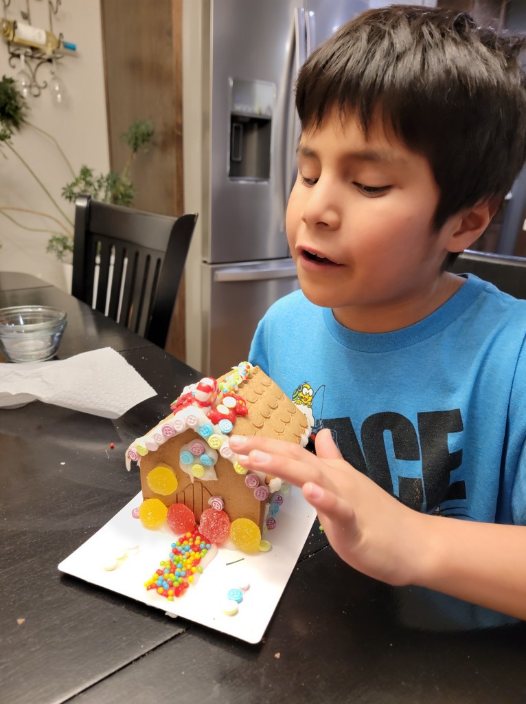 Little boy using his hands to look at a gingerbread house he made