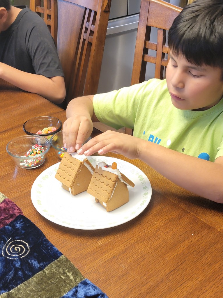 One boy adding candies to the top of his gingerbread roof.