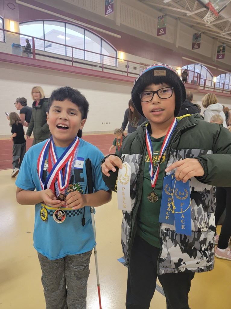 Two boys showing there medals and ribbons. One boy has a cane tucked under his arm.