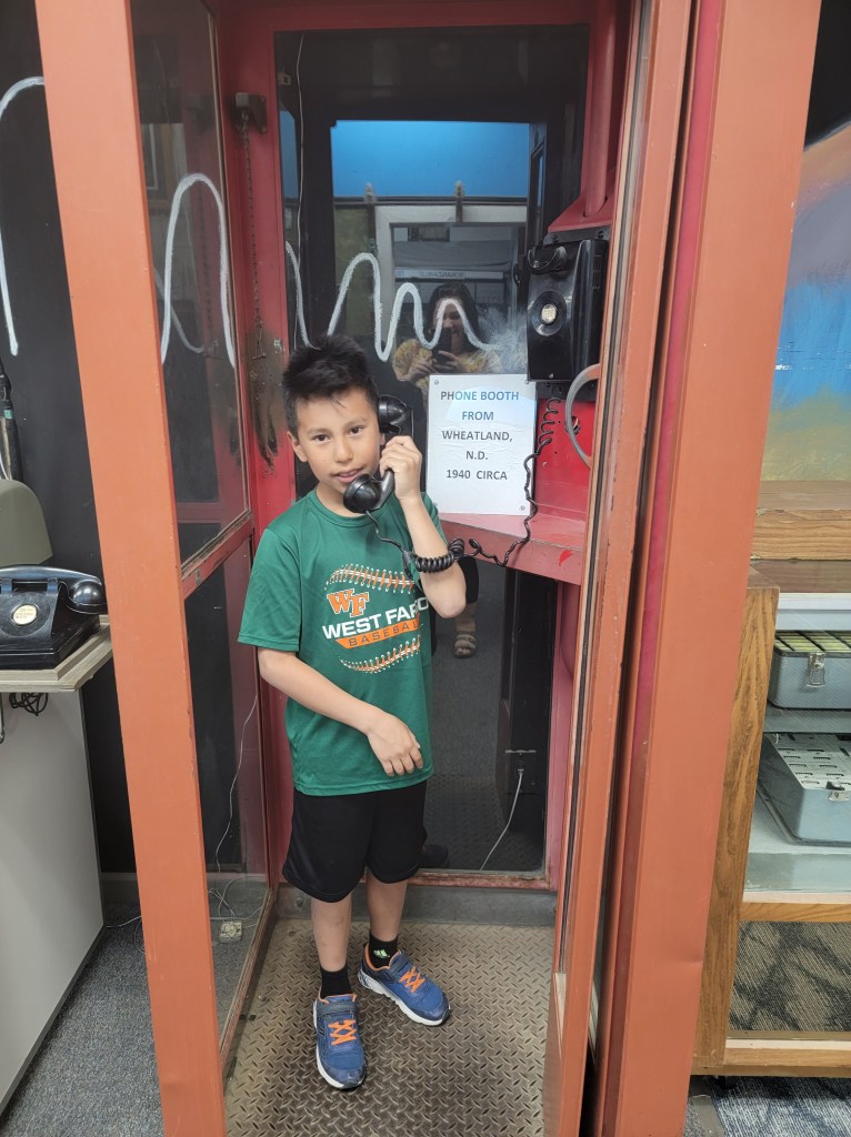 Young boy standing in an old telephone booth, holding the receiver up to his ear. 
