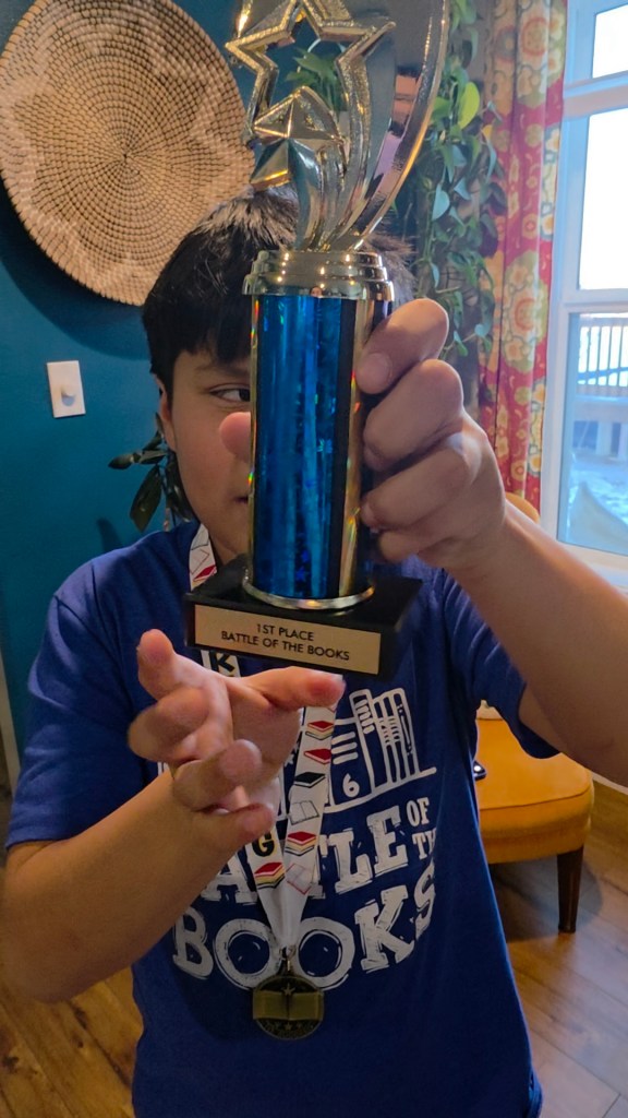 Boy wearing a blue shirt and a medal holding a trophy that says first place on it.